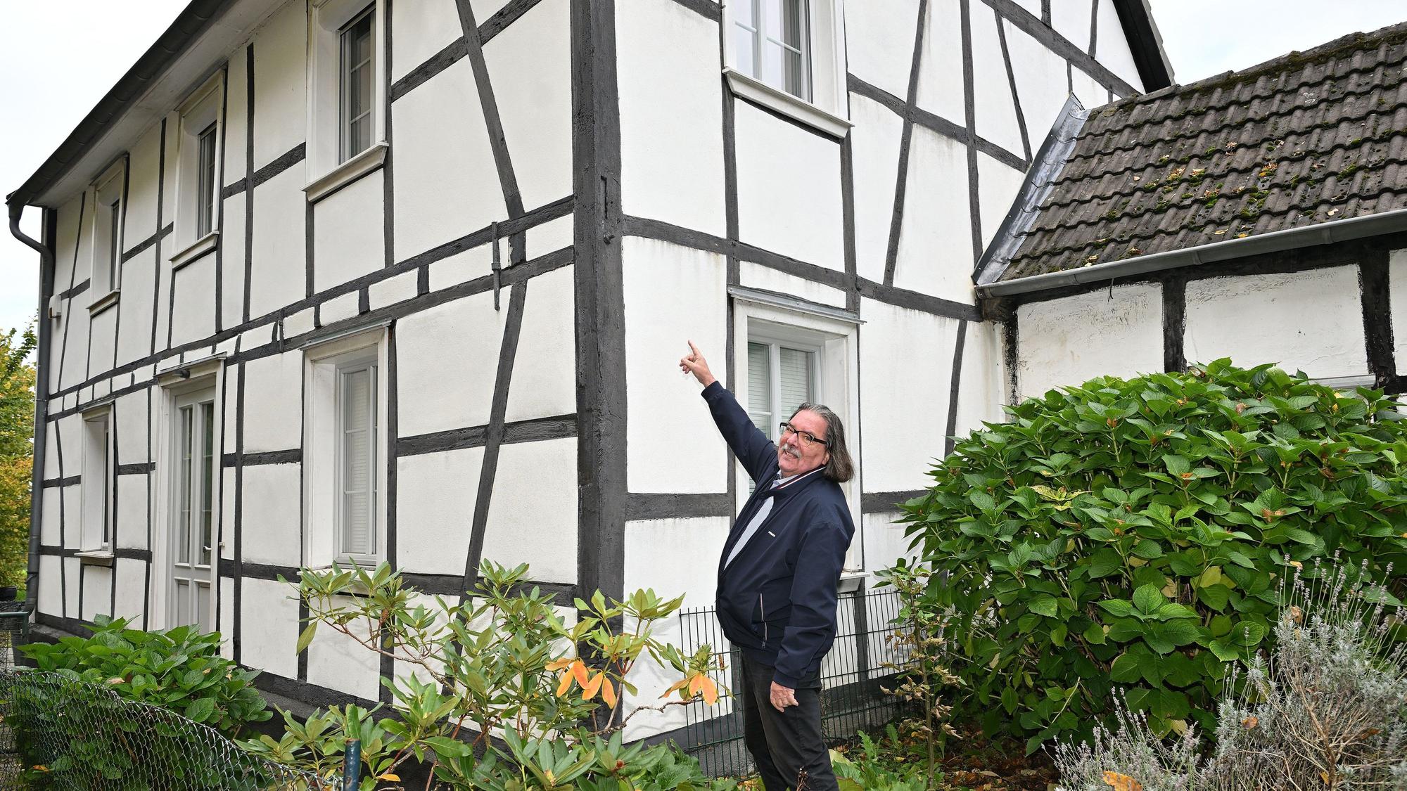 Ein Mann deutet auf die Außenbalken eines bergischen Fachwerkhauses.