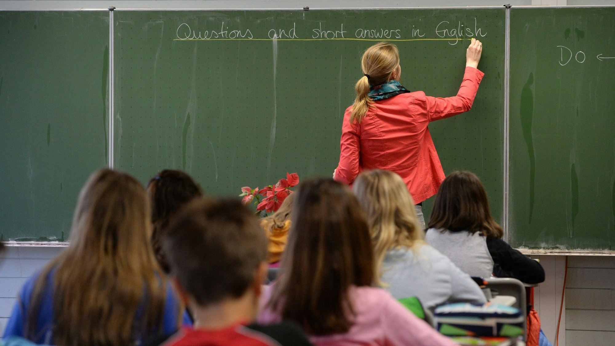 Eine Frau schreibt in einem Klassenzimmer eines Gymnasiums während des Englischunterrichts in einer 5. Klasse an die Tafel.