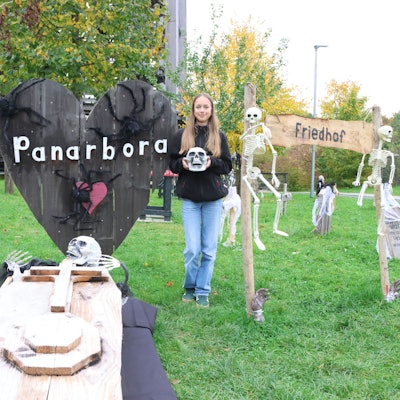 Eine Frau steht im Geisterpark Panarbora, neben Gruselelementen auf einer Wiese.