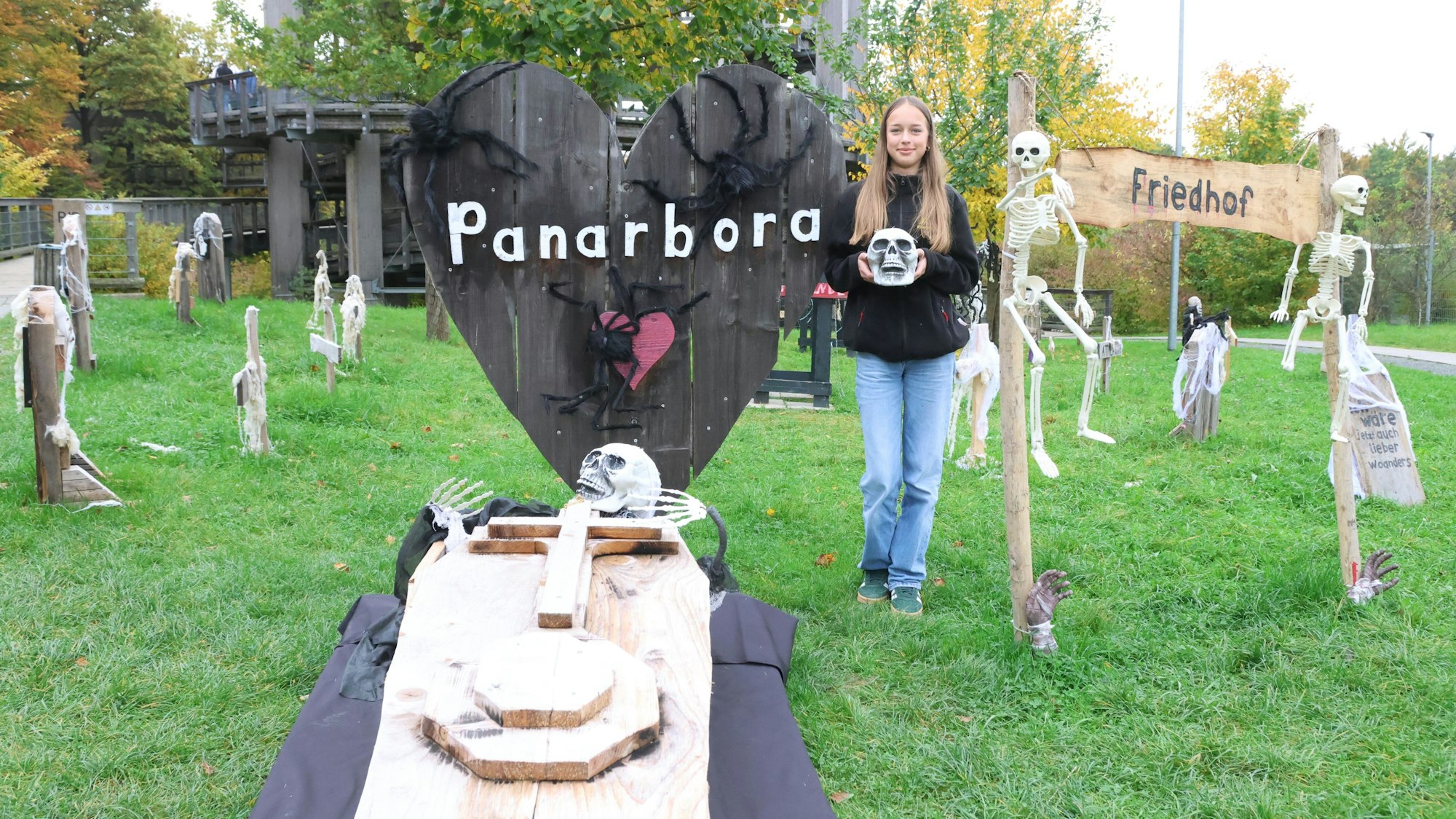 Eine Frau steht im Geisterpark Panarbora, neben Gruselelementen auf einer Wiese.