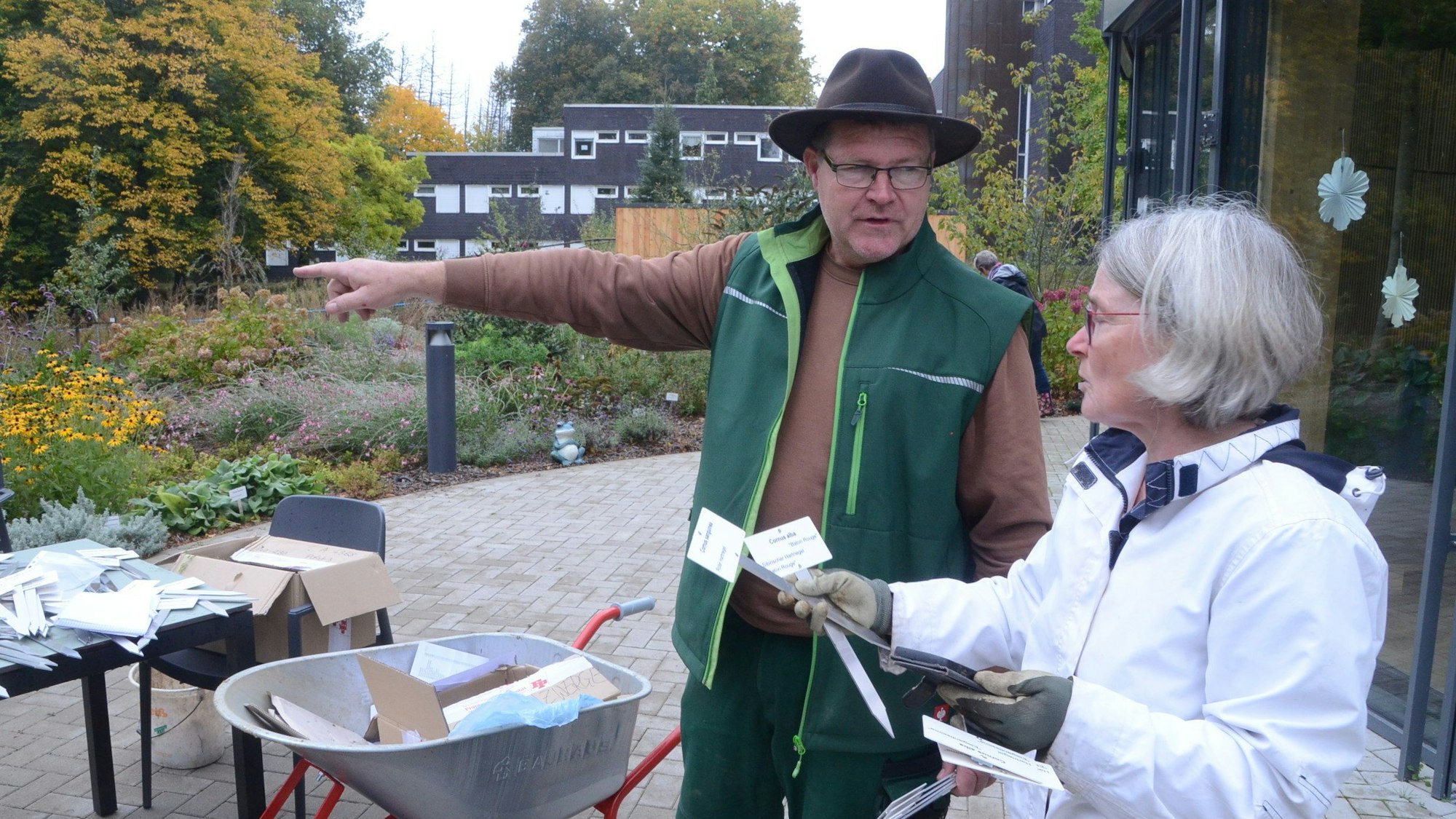Ein Mann mit grüner Weste und Hut steht neben einer Frau in einer weißen Jacke.