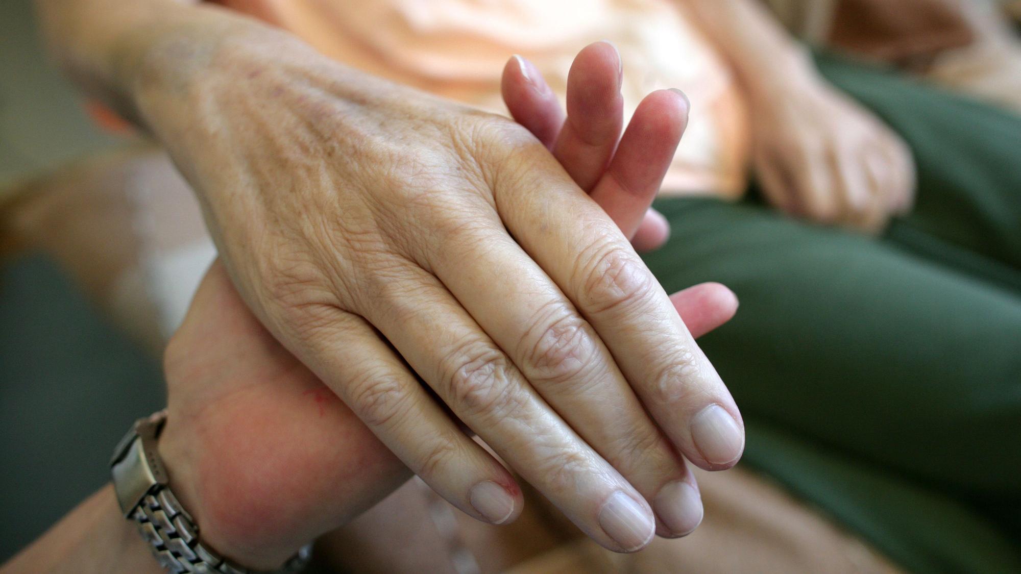 Die Hand einer kranken Frau wird gehalten.