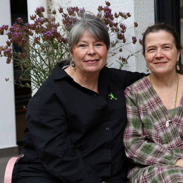 Goldschmiedin Ursula Palm-Zumbé und Künstlerin Annette von der Bey sitzen nebeneinander auf einer Bank vor einem Schaufenster.