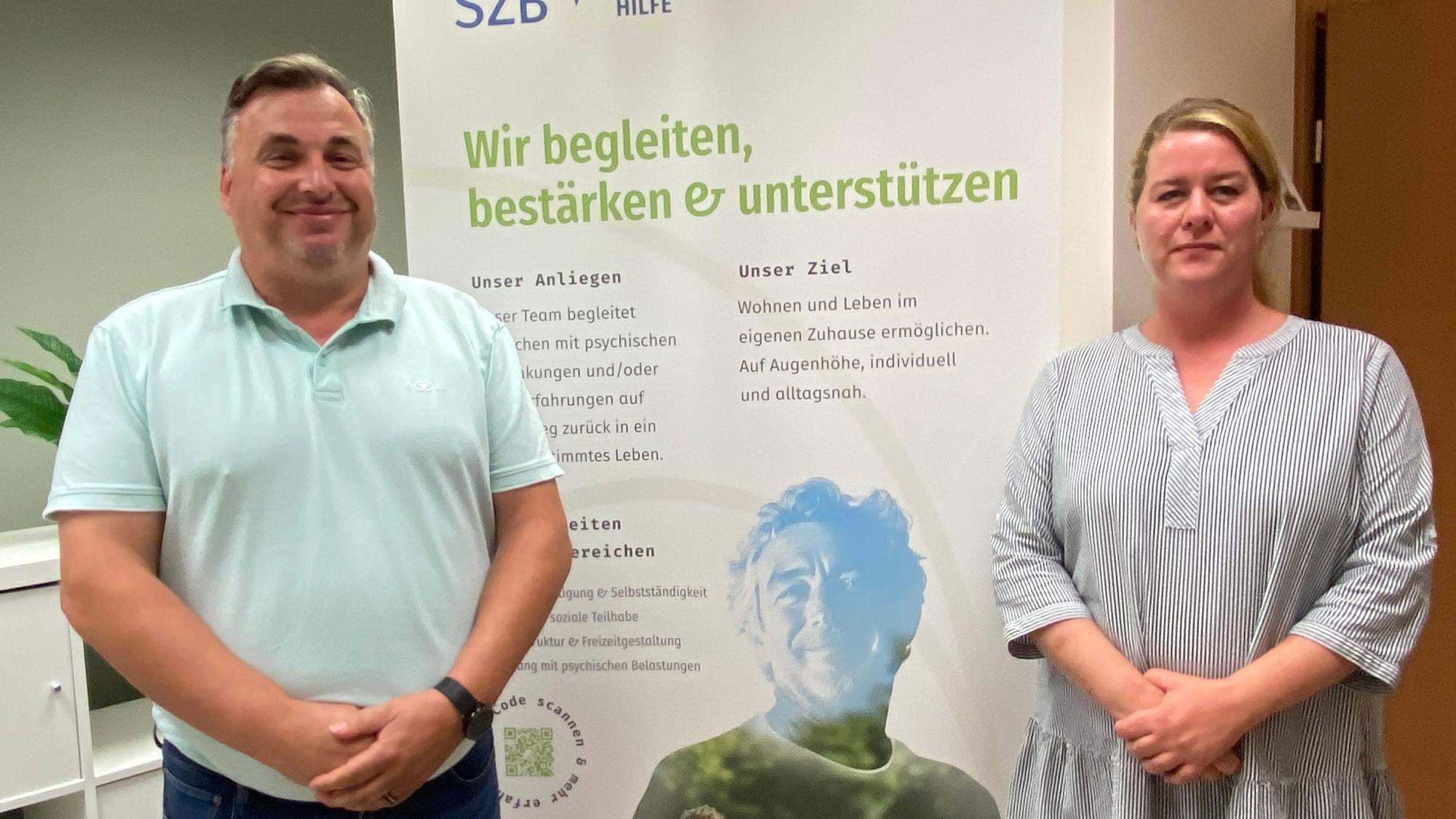 Thomas Sohr und Jessica Breitbarth stehen vor einem Banner, auf dem die SZB für ihre Angebote wirbt.