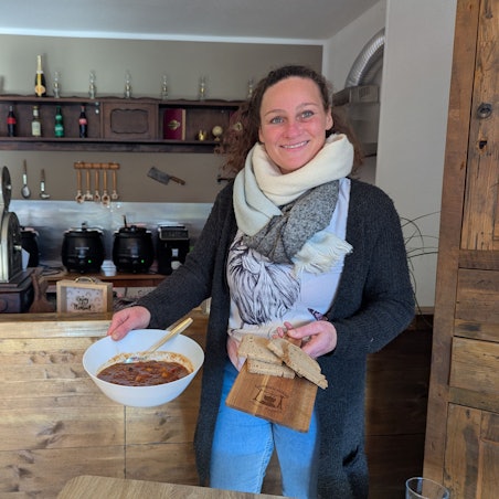 Das Foto zeigt die Inhaberin mit einer Terrine Suppe und Brot vor der Theke der Gaststätte.