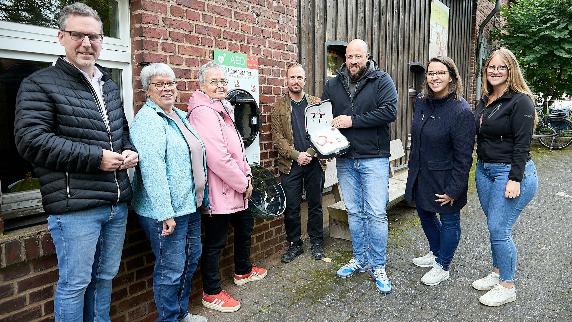 Drei Männer und vier Frauen stehen am Haus der Fossilien in Nettersheim, wo ein Defibrillator angebracht wurde.