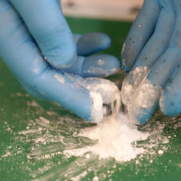 Ein Mann hebt mit blauen Handschuhen einen kleinen Teil von Kokainpulver hoch.