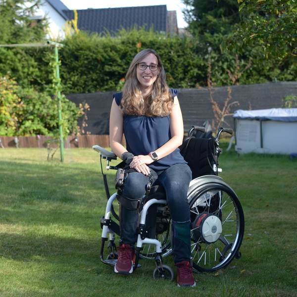 Die Autorin sitzt in einem Garten im Rollstuhl und lächelt in die Kamera.