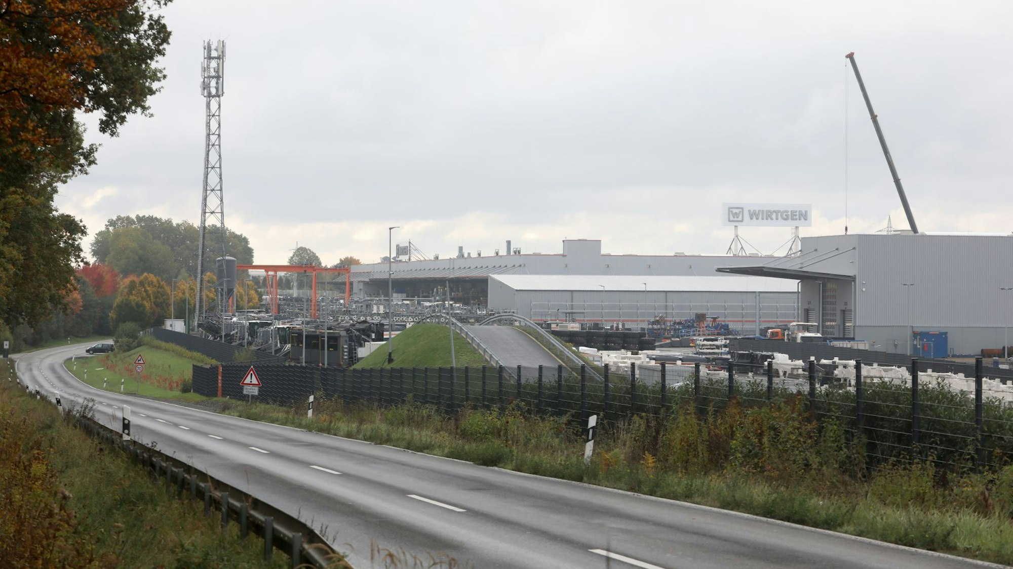 Blick auf ein großes Werksgelände, im Vordergrund verläuft eine zweispurige Straße.
