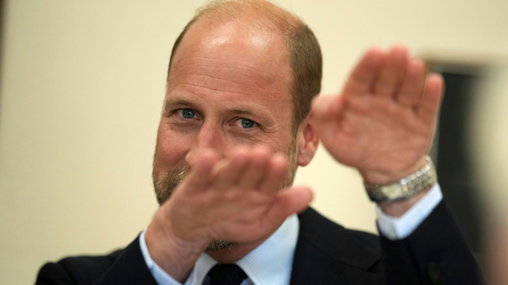 Prinz William lächelt und gestikuliert mit verschwommenen Händen im Vordergrund