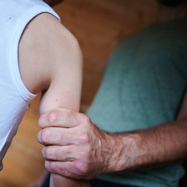 Das Symbolbild zeigt in einer gestellten Szene, wie ein Mann ein Kind am Arm festhält. Zu sehen sind nur Körperausschnitte.