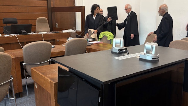 Der Angeklagte mit seinen Verteidigern, Dolmetscher und Wachtmeister im Landgericht Köln. Im Vordergrund die genutzte Videoanlage zur Übertragung der Vernehmung in einen anderen Saal.