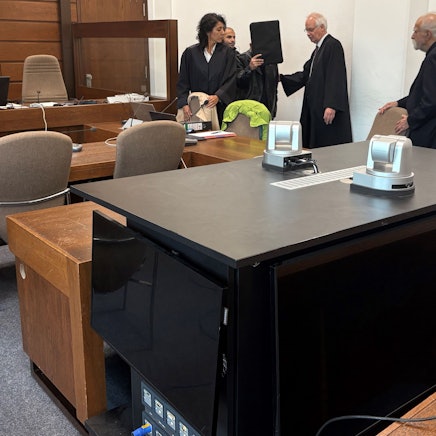 Der Angeklagte mit seinen Verteidigern, Dolmetscher und Wachtmeister im Landgericht Köln. Im Vordergrund die genutzte Videoanlage zur Übertragung der Vernehmung in einen anderen Saal.