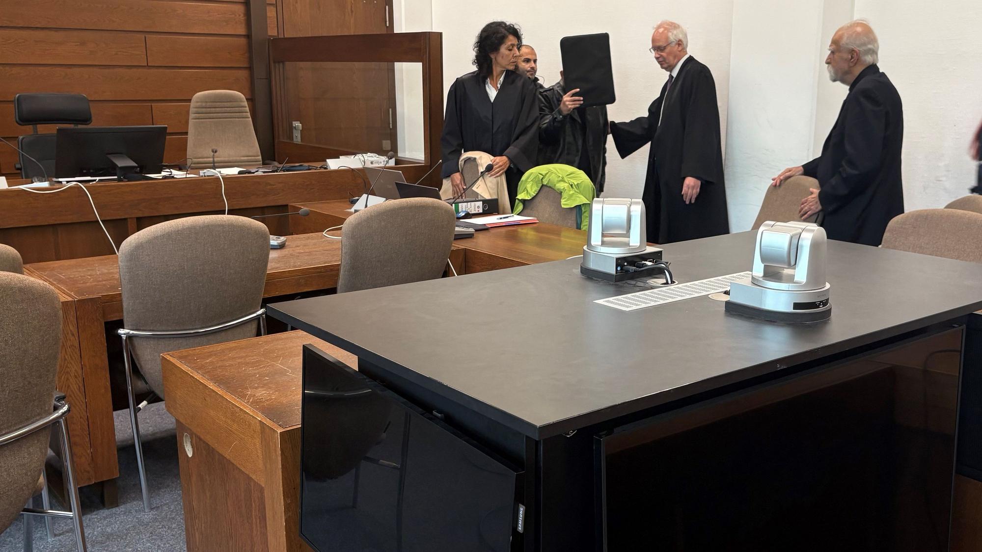 Der Angeklagte mit seinen Verteidigern, Dolmetscher und Wachtmeister im Landgericht Köln. Im Vordergrund die genutzte Videoanlage zur Übertragung der Vernehmung in einen anderen Saal.