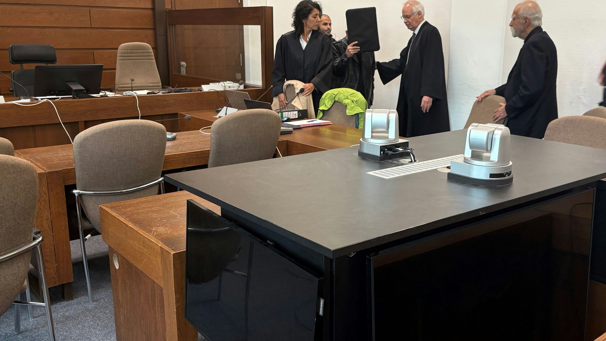 Der Angeklagte mit seinen Verteidigern, Dolmetscher und Wachtmeister im Landgericht Köln. Im Vordergrund die genutzte Videoanlage zur Übertragung der Vernehmung in einen anderen Saal.