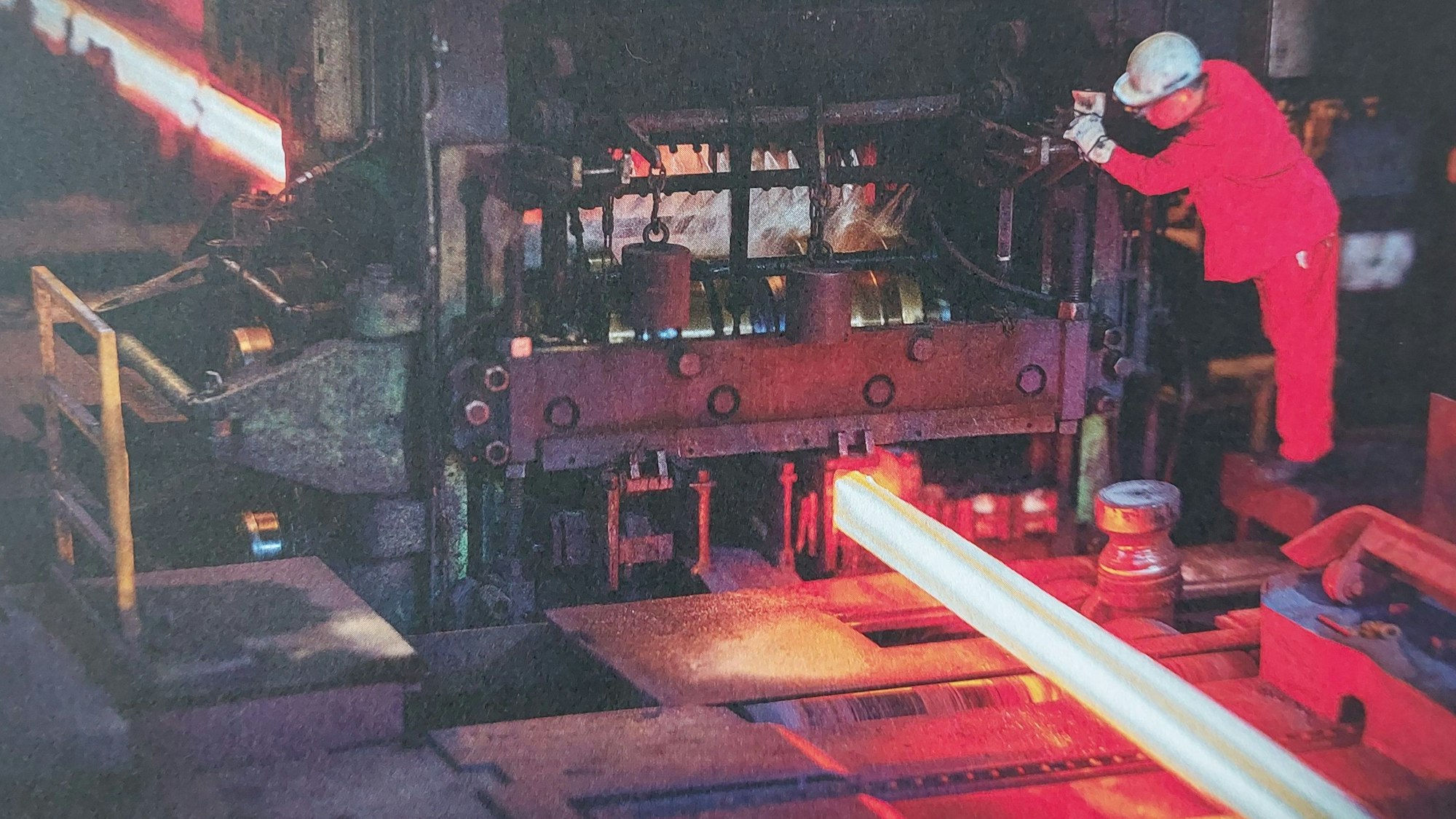 Ein Mann im roten Overall bedient eine Maschine in einer Fabrik.