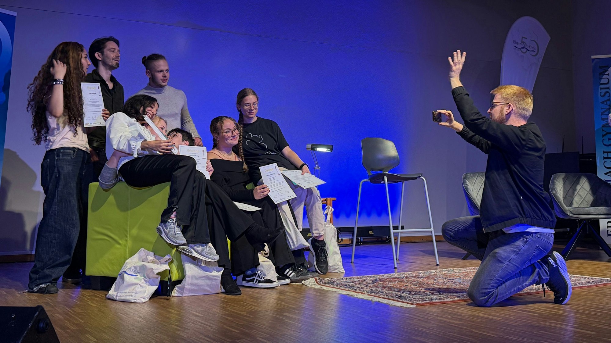 Das Foto zeigt eine Gruppe von Jugendlichen, die sich gerade von einem Mann mit dem Smartphone fotografieren lässt.