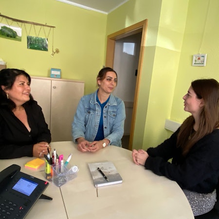 Drei Frauen sitzen an einem Tisch und unterhalten sich.