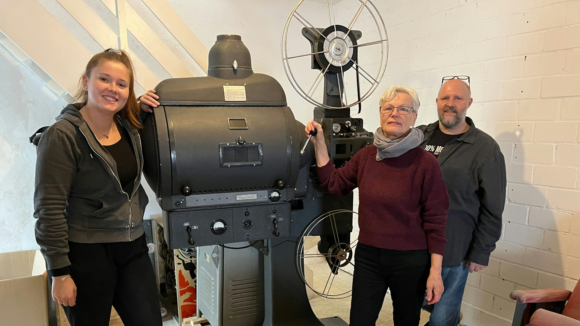Das Foto zeigt zwei Frauen und einen Mann vor dem historischen Filmprojektor.