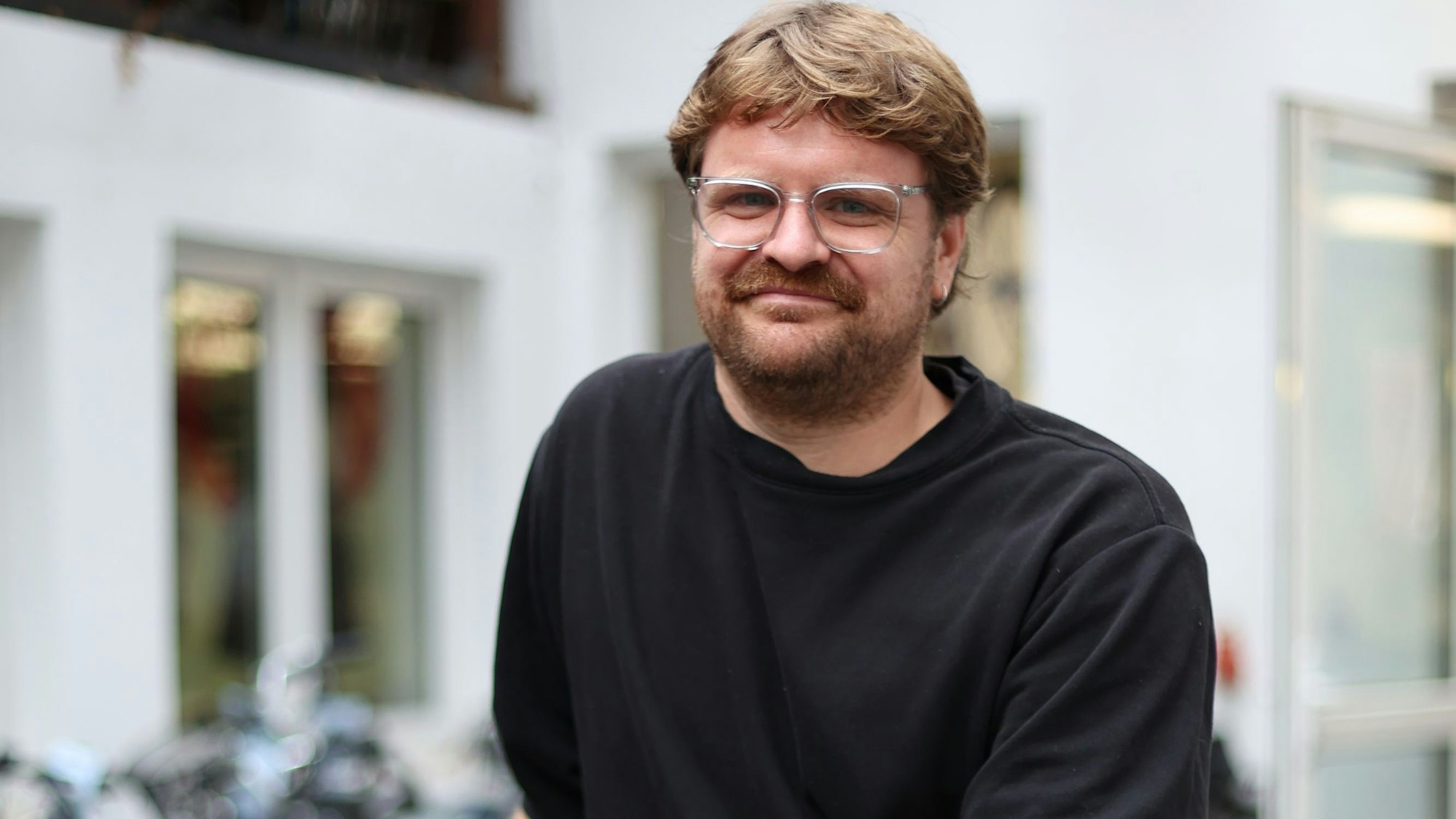 Ein Mann mit Brille, Bart und schwarzem Pulli hält ein Fahrrad.