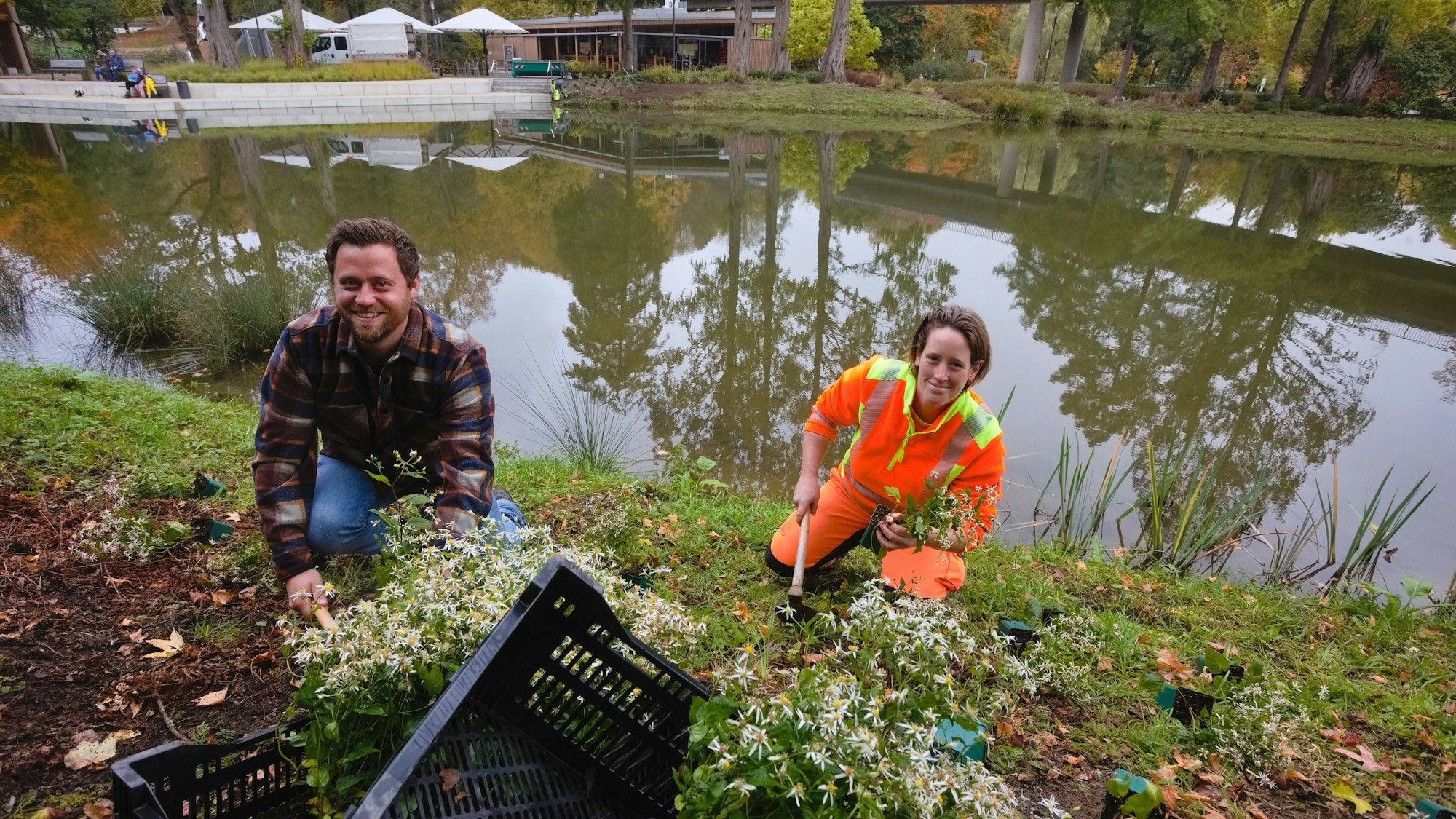 Ein Mann und eine Frau setzen Pflanzen am Ufer eines Teichs.