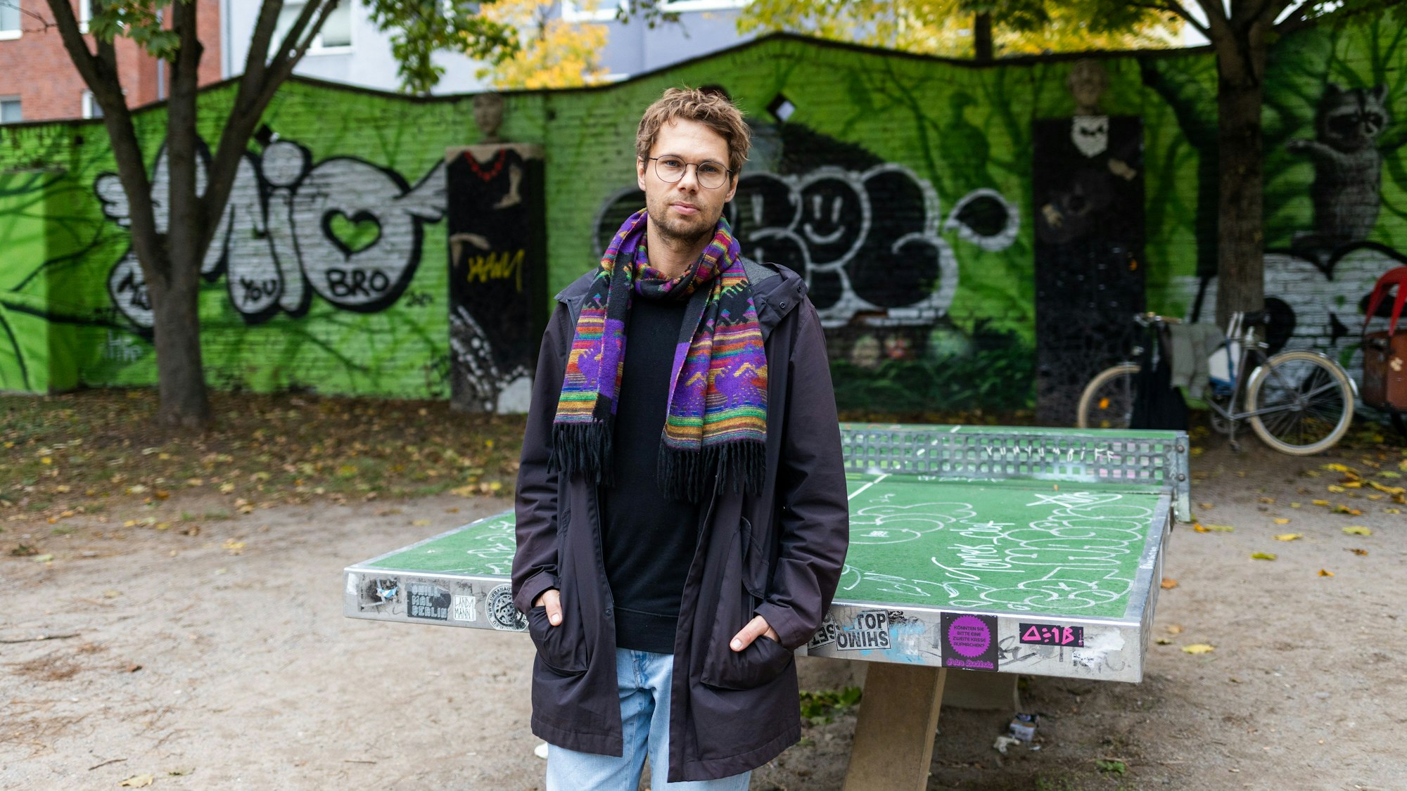 Ein Mann mit lila Schal steht vor einer Tischtennisplatte.