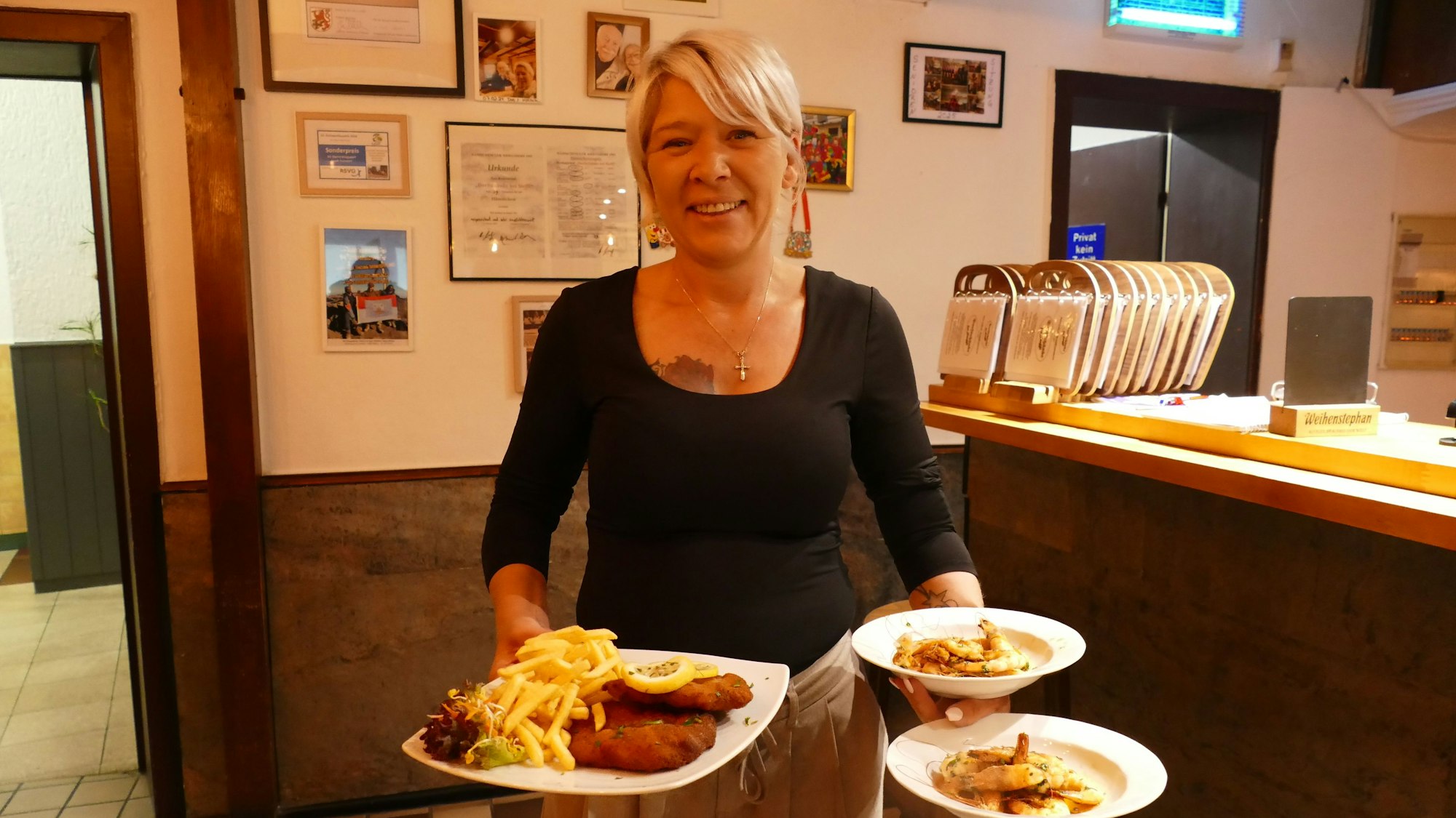 Eine Frau trägt drei Teller mit Speisen.