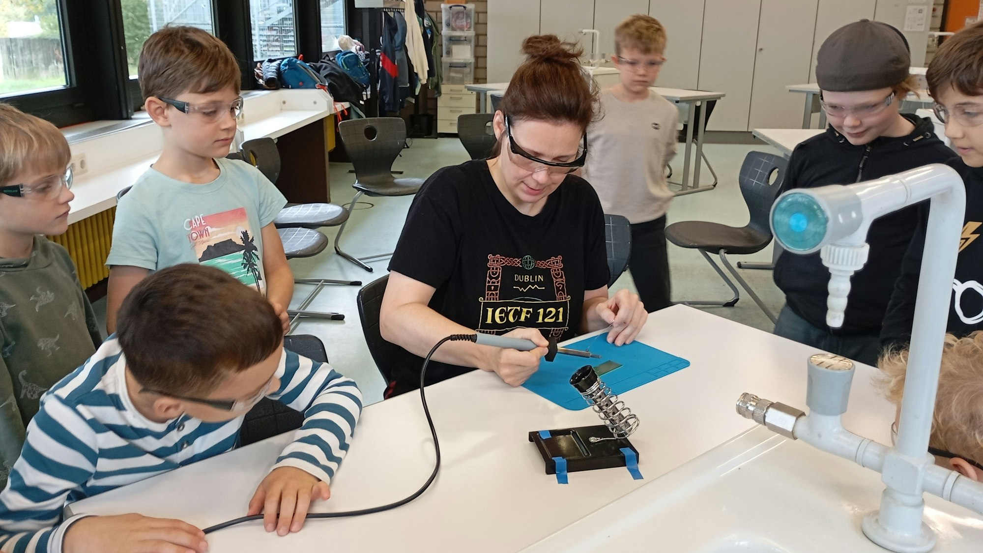 Das Foto zeigt eine Lehrerin, die Kindern das Löten beibringt.