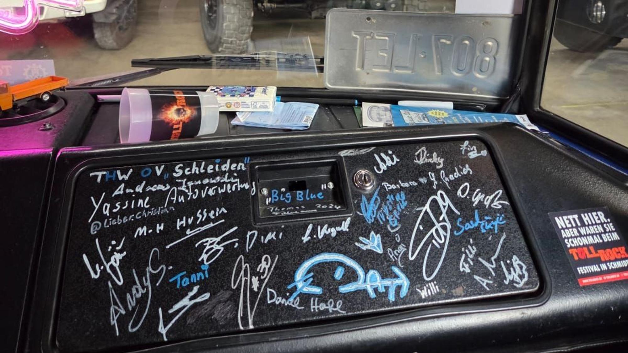 Auf einer schwarzen Kunststoff-Verkleidung im Führerhaus eines Lkw sind zahlreiche Autogramme.