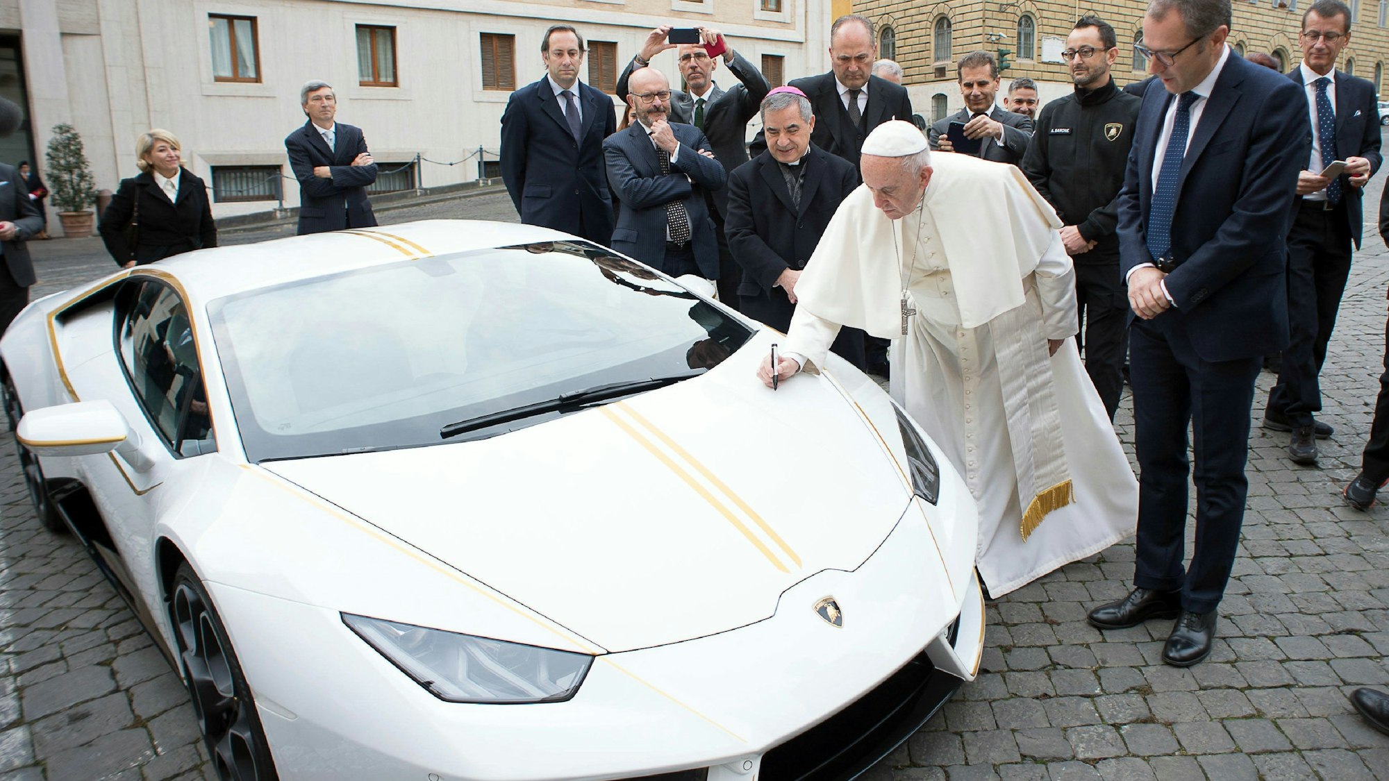 Das Bild zeigt Papst Franziskus vor einem weißen Lamborghini, der ihm vom italienischen Sportwagenhersteller geschenkt wurde. Foto: L'Osservatore Romano/AP/dpa