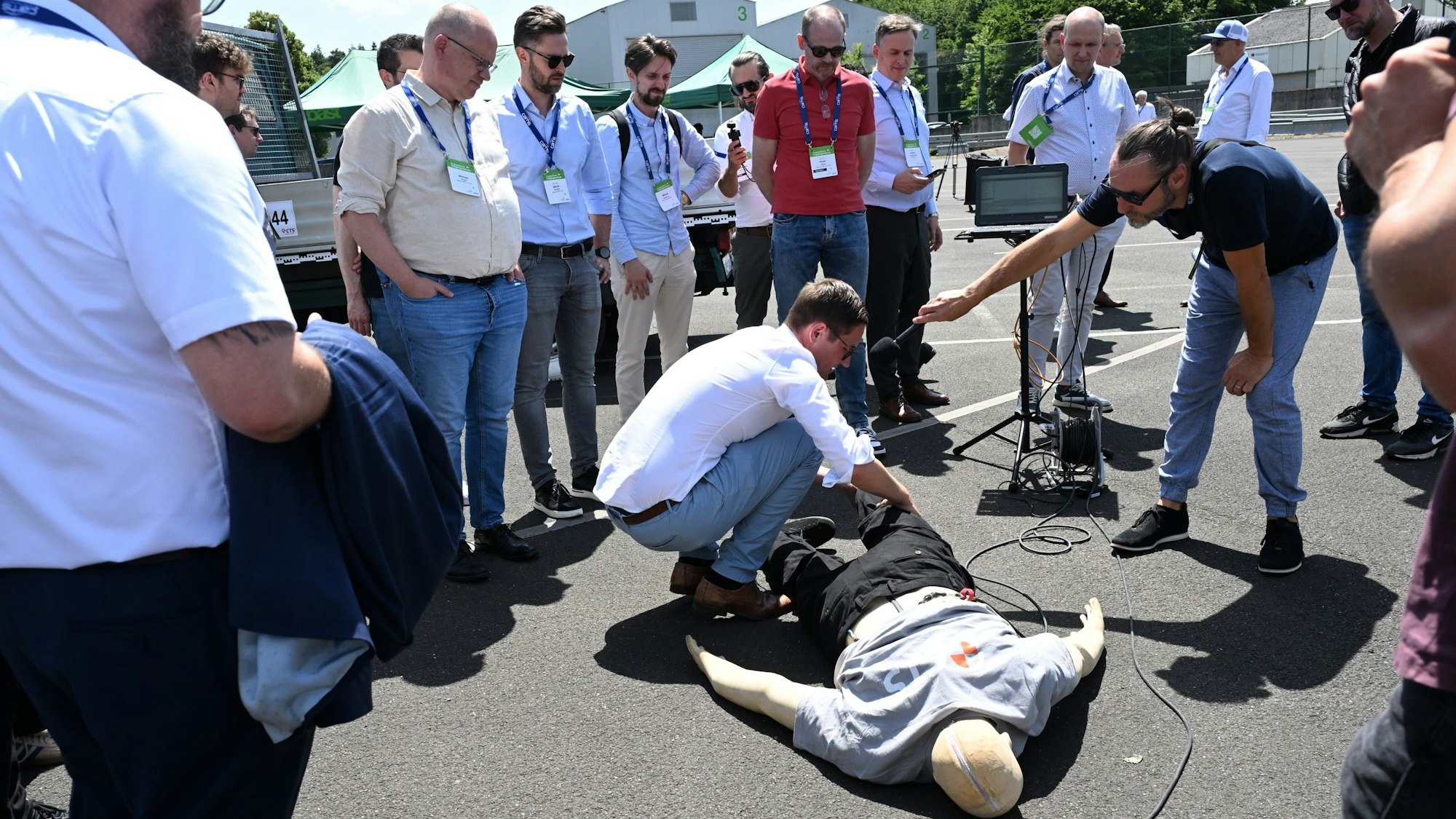 Sicherheitsexperten aus aller Welt stehen nach einem Crashtest um den am Boden liegenden Dummy.