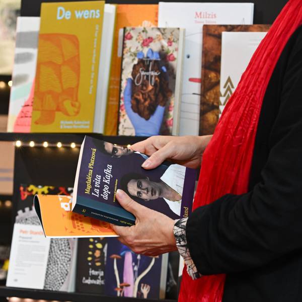 Eine Person hält Bücher in der Hand und steht vor einem Bücherregal.