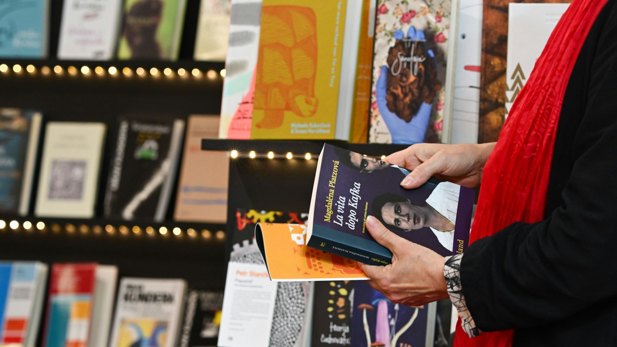 Eine Person hält Bücher in der Hand und steht vor einem Bücherregal.