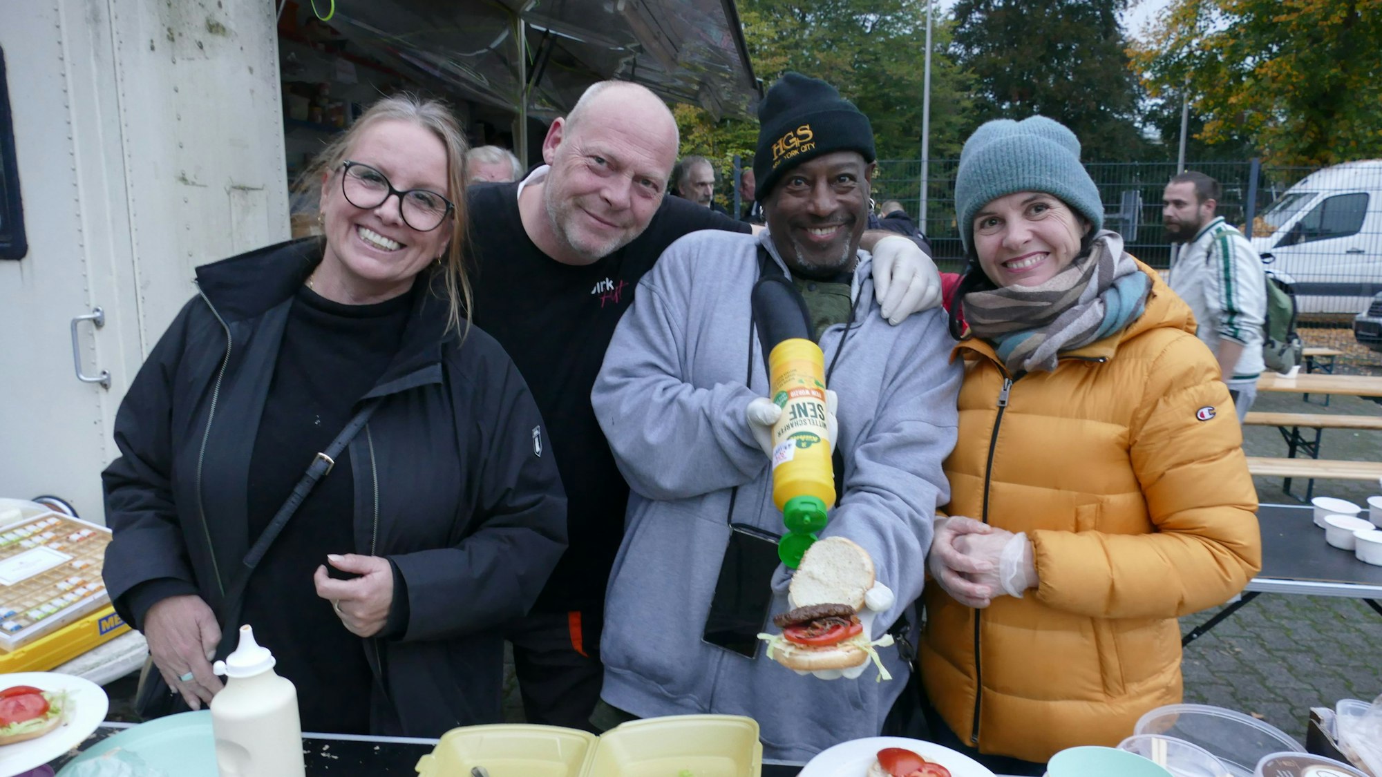 Männer und Frauen stehen an einem Tisch und bereiten Burger zu.