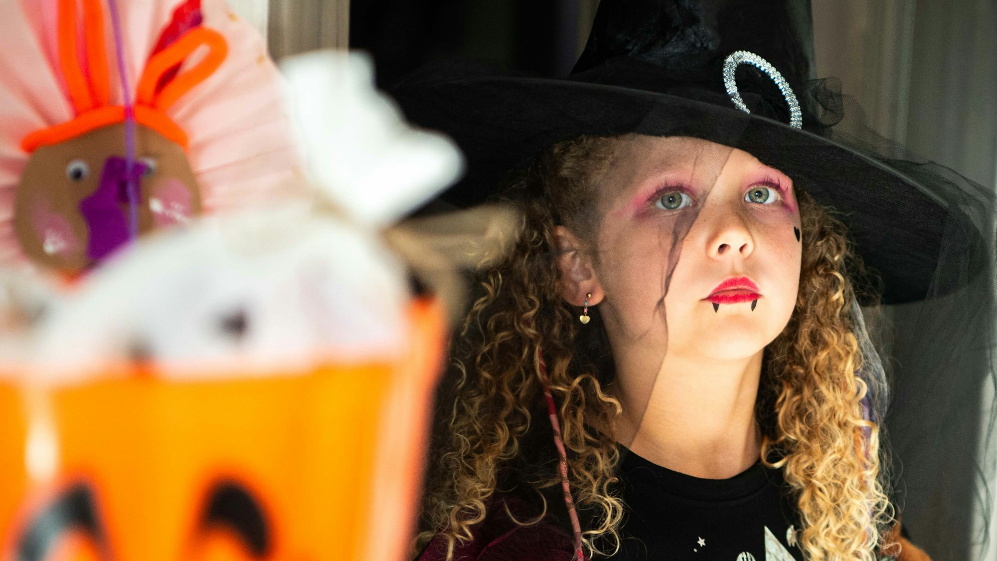 Ein Kind ist als Hexe verkleidet, im Vordergrund steht ein Kürbisbehälter.