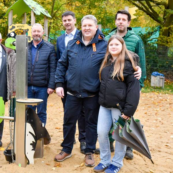 Männer und Frauen stehen nebeneinander auf einem Spielplatz vor Spielgeräten und lächeln.