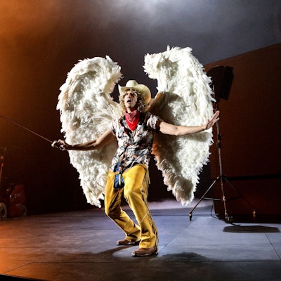 Lavinia Nowak steht auf einem Gabelstapler und betätigt einen Flammenwerfer, Frank Genser trägt große Engelsflügel und Cowboyhut