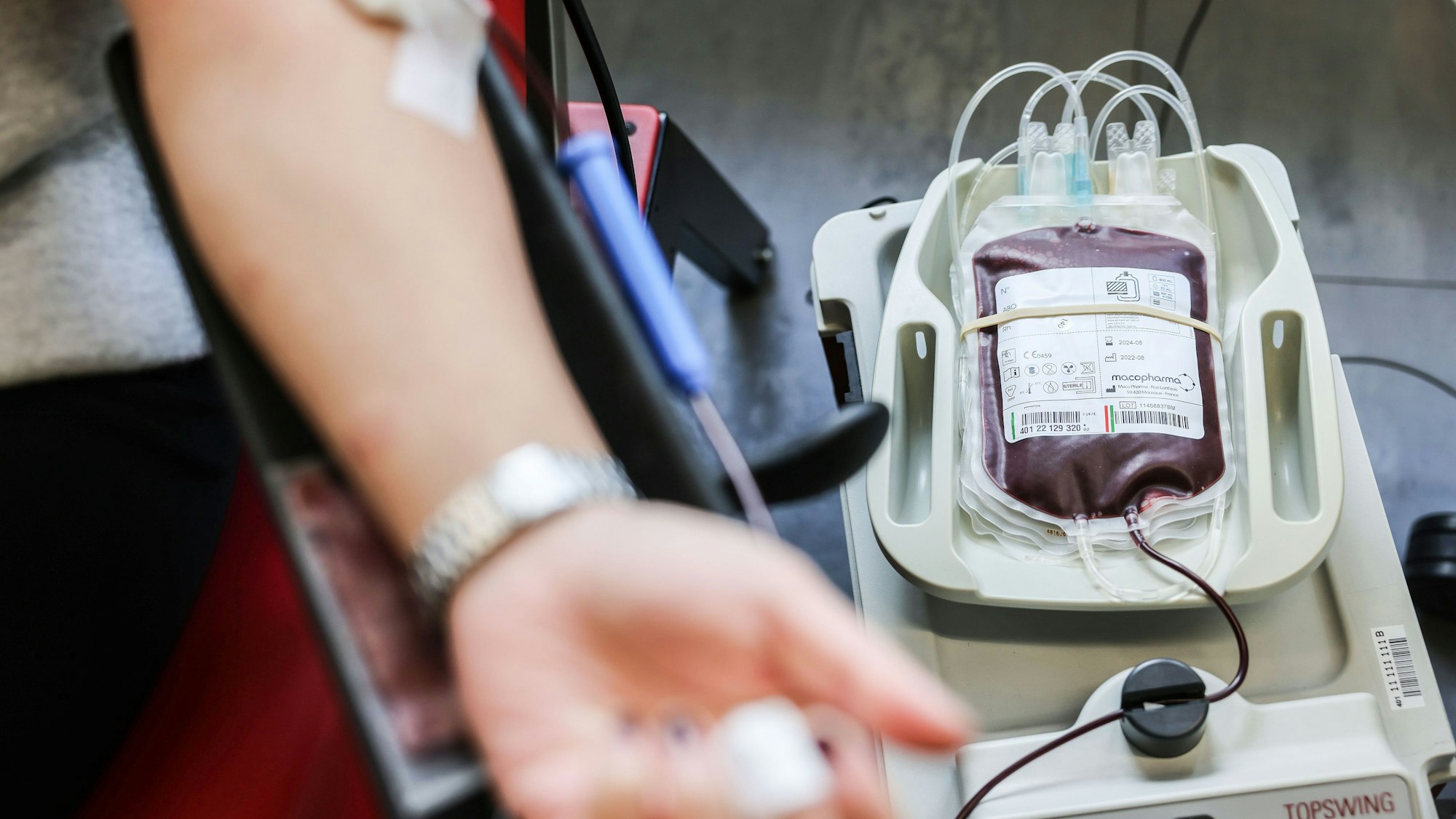 Das Symbolbild Bild zeigt einen Arm mit einer Kanüle in der Vene. Daneben liegt ein Beutel mit Blut.