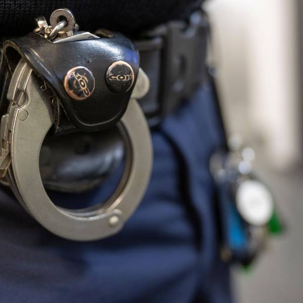 Eine Handschelle hängt am Gürtel eines Polizisten.