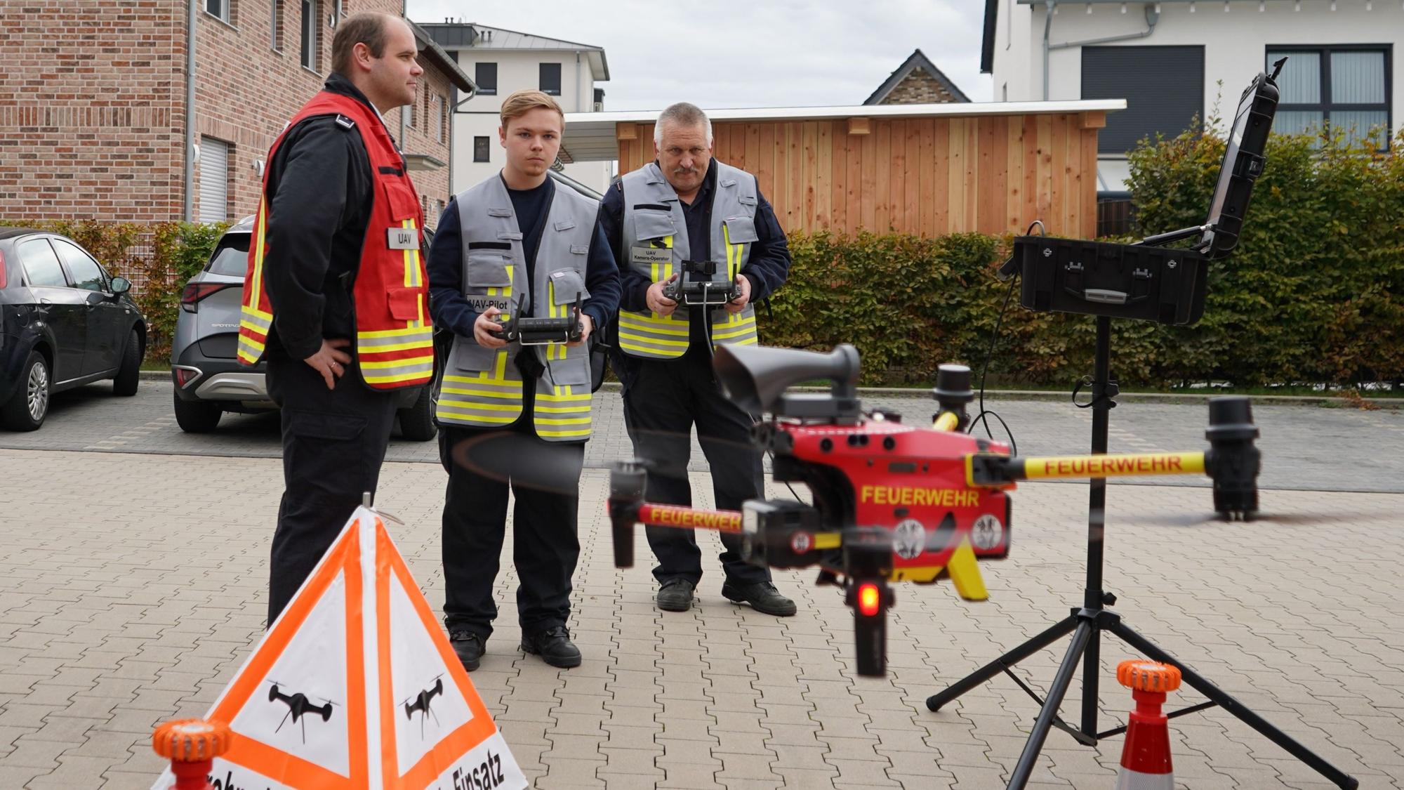 Das Foto zeigt drei Einsatzkräfte der Feuerwehr beim Fliegen einer Drohne.