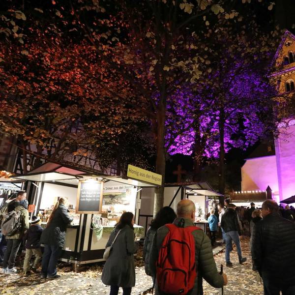 Menschen an mehreren Marktbuden, im Hintergrund eine von Scheinwerfern angestrahlte Kirche.