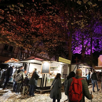 Menschen an mehreren Marktbuden, im Hintergrund eine von Scheinwerfern angestrahlte Kirche.