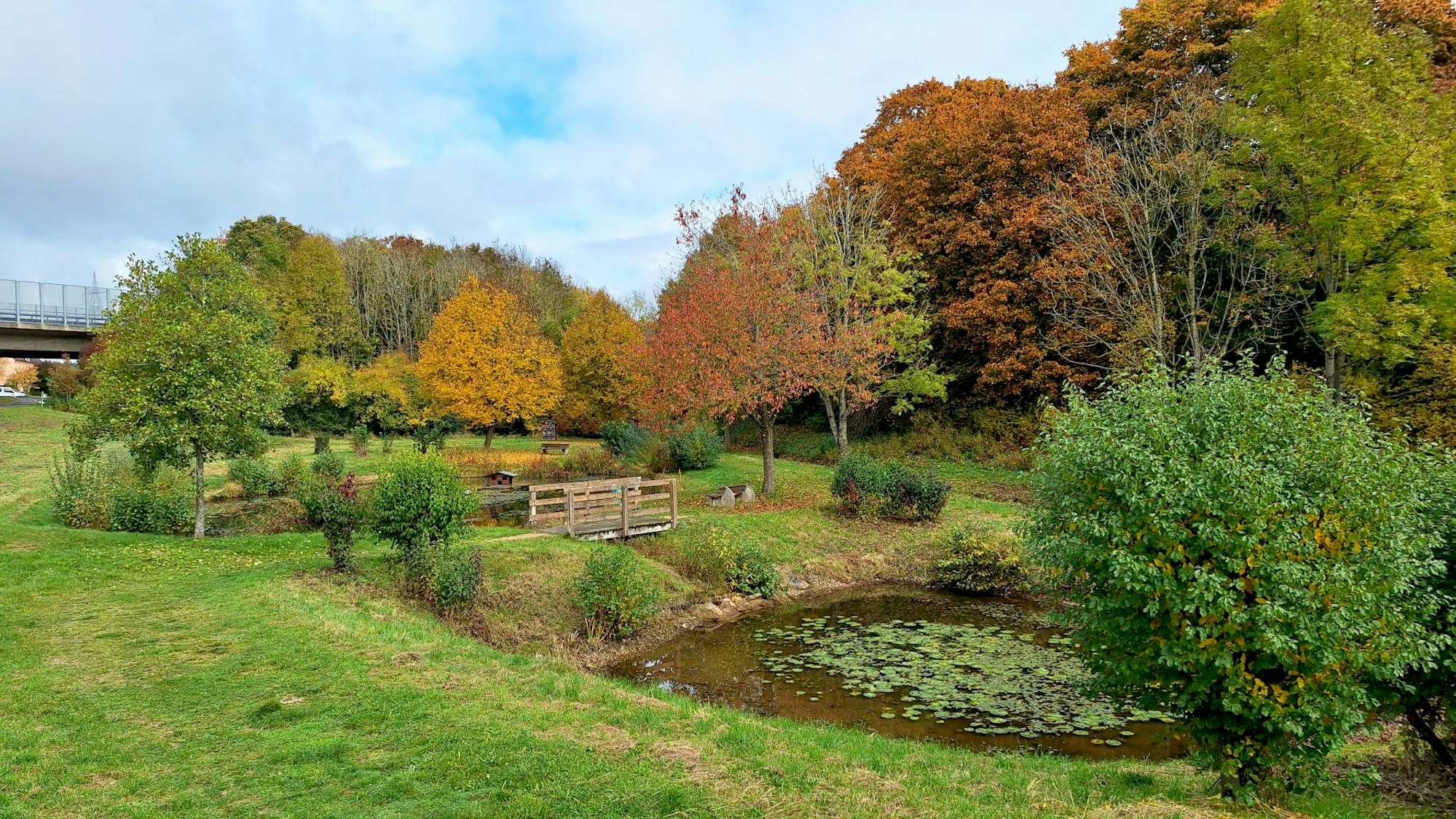 In der Herbstlandschaft sieht man den kleinen Königsee, in dessen Mitte ein Steg verläuft.