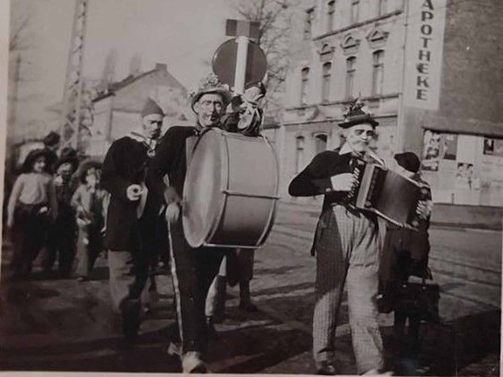 Straßen Karneval in Höhenberg auf der Olpener Straße 1953 mit einem sog. Zöchelche. So nannte man privat organisierte Musiktrupps mit zufällig gewürfelten „Jecken “, die fröhliche Lieder für alle anstimmten. Kinder marschieren begeistert mit.