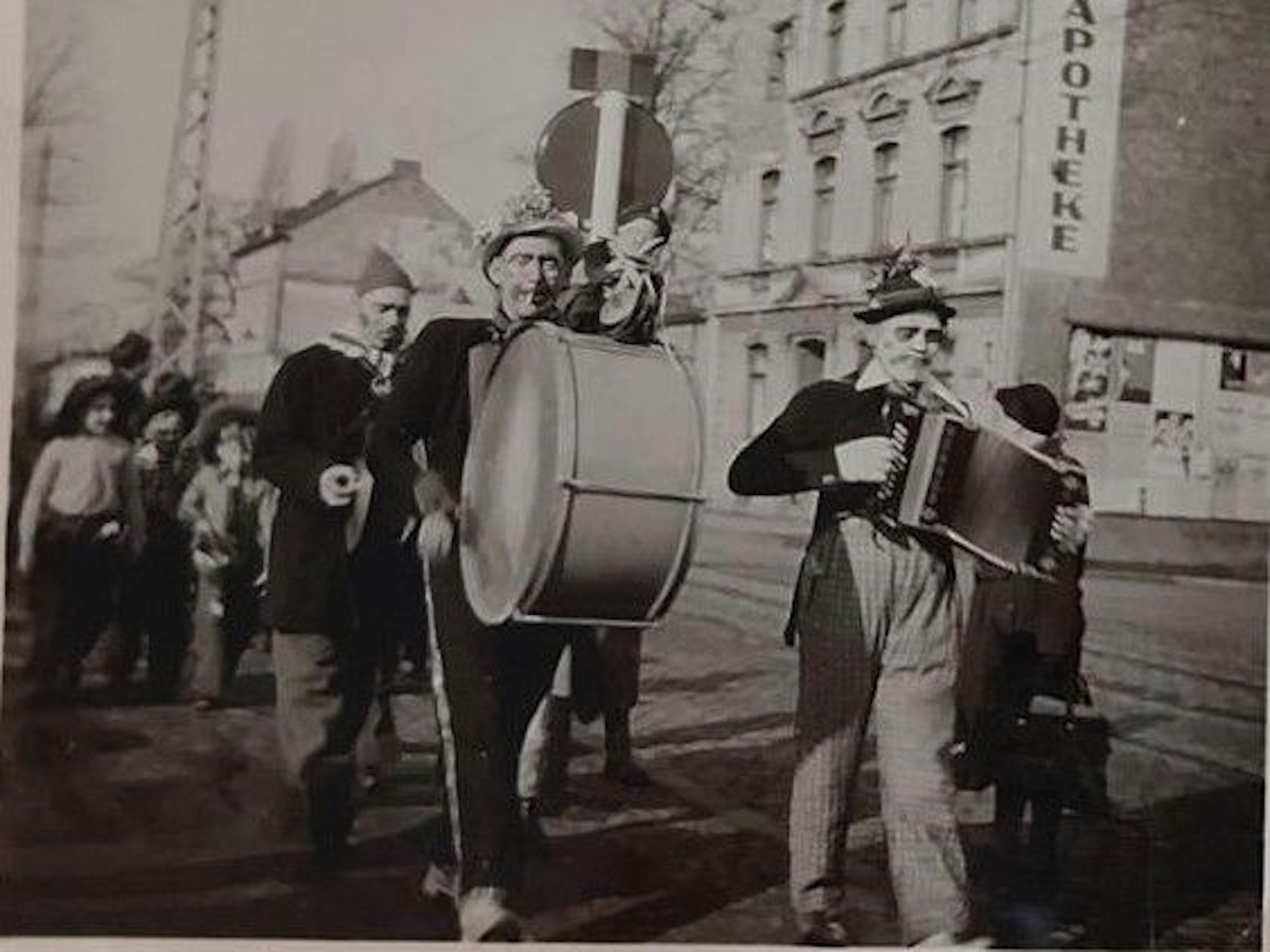 Straßen Karneval in Höhenberg auf der Olpener Straße 1953 mit einem sog. Zöchelche. So nannte man privat organisierte Musiktrupps mit zufällig gewürfelten „Jecken “, die fröhliche Lieder für alle anstimmten. Kinder marschieren begeistert mit.