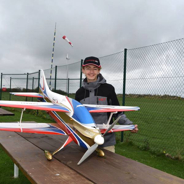 Marian Friedrich steht hinter seinem Modellflugzeug, ein weißer Doppeldecker mit blauen, roten und goldenen Akzenten.
