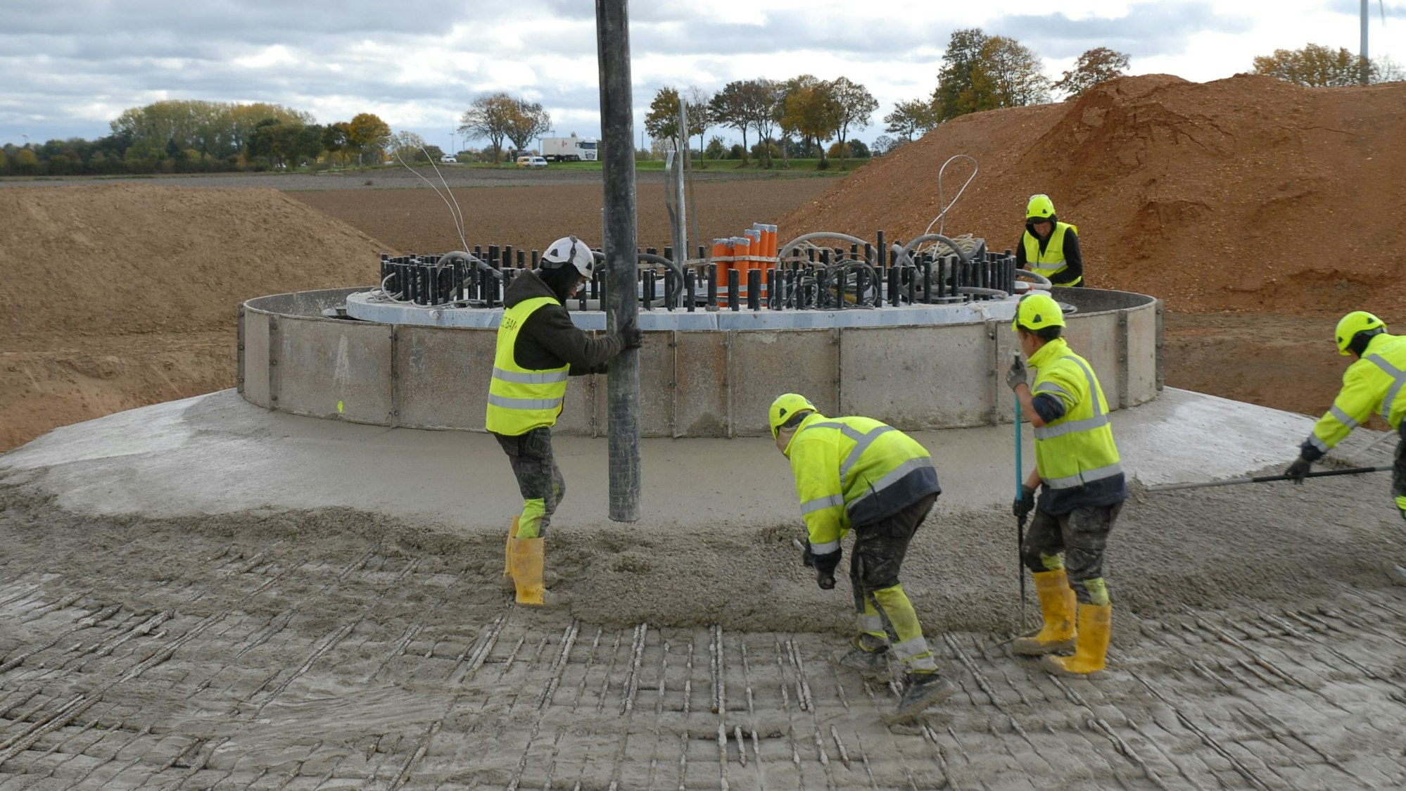 Zu sehen sind Menschen in Arbeitskleidung, die das Fundament eines Windrades gießen.