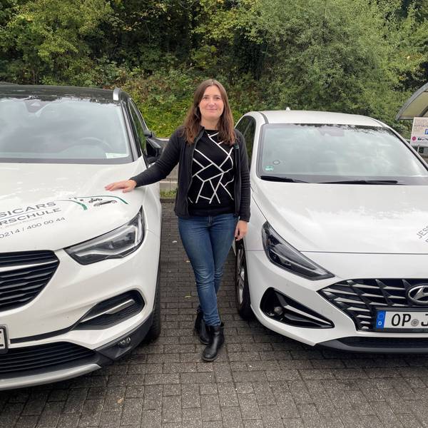 Jessica Richartz steht zwischen zwei Fahrschulautos.