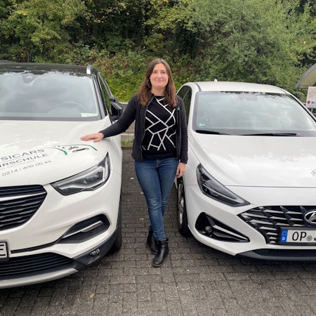 Jessica Richartz steht zwischen zwei Fahrschulautos.