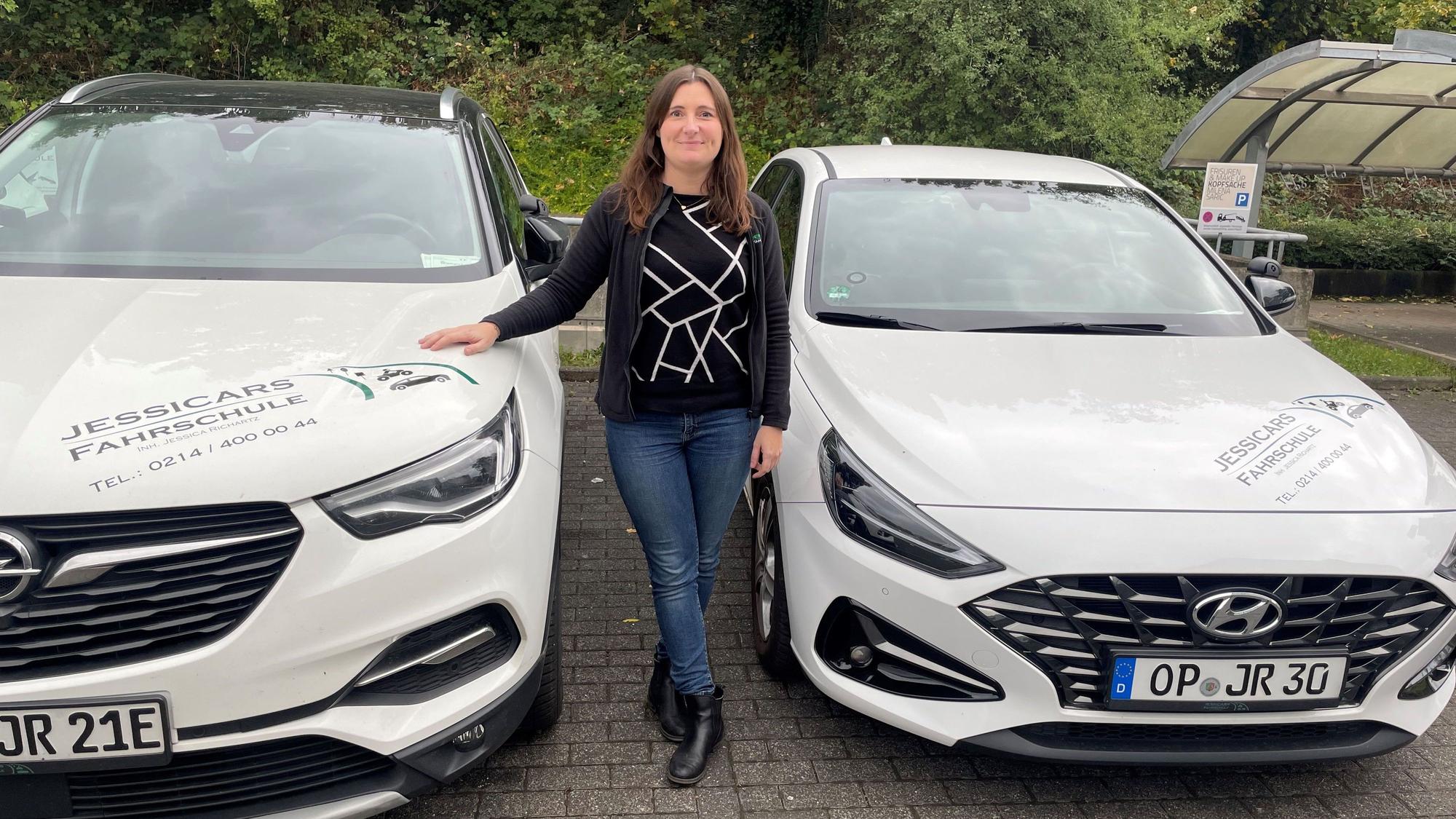 Jessica Richartz steht zwischen zwei Fahrschulautos.